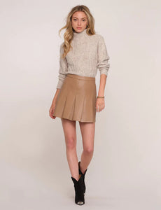 Model wearing Heartloom Ami Skirt in the colour "Desert": A camel-coloured pleated vegan leather a-line skirt. Featured with Heartloom Thames sweater and black western booties.