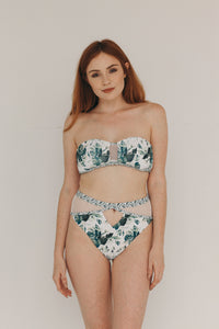UNIKONCEPT Lifestyle boutique: Model is wearing a white strapless somedays loving bikini top. The emerald oasis bandeau top comes in a tropical greenery print, with a key hole of mesh fabric at the bust.