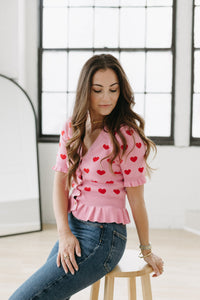 UNIKONCEPT Lifestyle Boutique and Lounge:Model wearing the Corazon Peplum Cardi by English Factory in Pink - a pink button up short sleeve peplum top with red hearts.