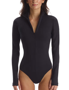UNIKONCEPT Shoppe & Lounge: The model is wearing the Neoprene Zip Long Sleeve Bodysuit by Commando. This black bodysuit has thumb holes and features raw cut edges. It has a quarter zip at the neckline with a collar and has a strap gusset closure. It is made from stretchy neoprene and hugs curves perfectly.