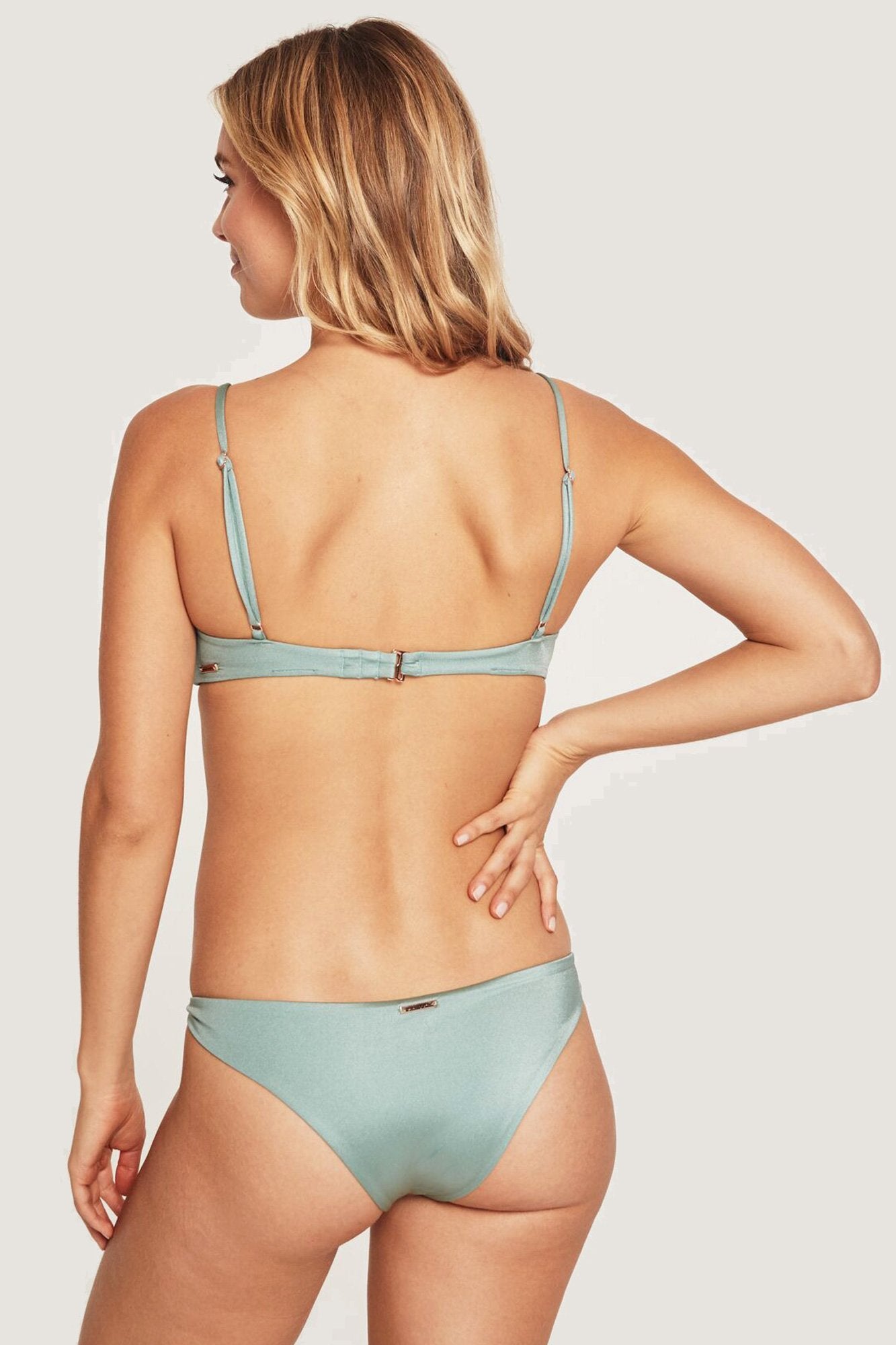 Back view of model wearing light, dusty green, low-rise spiritual gangster bikini bottoms. The Cozumel bikini bottoms in sage features a knotted side detail.