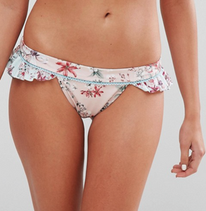 Front view of model wearing light pink Minkpink bikini bottoms. The sherbert cheeky frill bottom comes with a light blue and pink floral print, ruffle trimmed Side view of model wearing triangle bikini top in a blue on white floral print and a ruffle trim waist band.