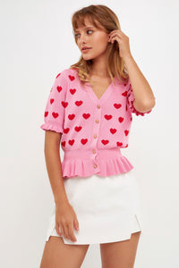  UNIKONCEPT Lifestyle Boutique and Lounge:Model wearing the Corazon Peplum Cardi by English Factory in Pink - a pink button up short sleeve peplum top with red hearts.